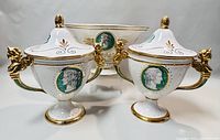 Front view of the two lidded urns with angel handles flanking the oval fruit bowl, showing overall design, classic medallions and gold accents