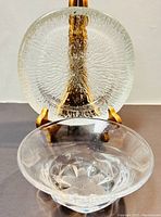 Crystal bowl in front with a textured glass iceberg ashtray displayed behind on wooden stands, showing the front and side views of the items.