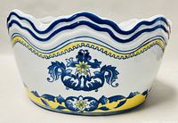 Front view of scalloped planter pot showing detailed blue and yellow floral patterns against white ceramic surface.