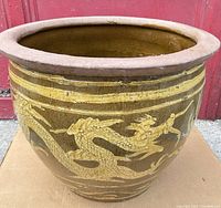 Front view of large heavy clay planter pot with raised yellow dragon design and brown glaze
