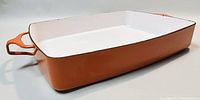 Photo of rectangular orange enamel lasagna baking dish with white enamel interior, integrated handles, minor wear visible.