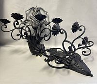 Pair of wrought iron 4-arm candleholder sconces shown lying on a surface, with clear view of flower-shaped candle holders and detailed scrollwork.
