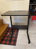 Full view of adjustable standing desk showing dark woodgrain rectangular top and black metal legs with adjustable height.