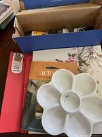 White flower-shaped paint palette with some paint residues, sitting on top of two painting instructional books.