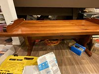 Front angled view of the hardwood coffee table showing the wood grain finish, raised curved edges, and sturdy leg supports.