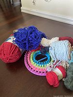 Photo showing various yarn bundles and two circular knitting looms on a dark wood floor