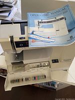 Husqvarna Prisma 950 sewing machine with multiple threads visible in front compartment and operating manual on top.