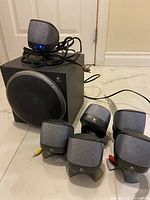 Full setup showing powered subwoofer and five satellite speakers with attached cables.