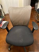Front view of office chair showing beige mesh backrest, black fabric seat, and armrests.