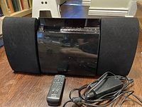 Front view of the Sony CD player, two speakers, remote control, and power supply on wooden floor.
