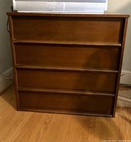 Front view of wooden dresser showing four drawers and one missing leg, scratches visible on top surface.