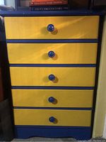 Photo of five drawer dresser with blue frame and yellow drawer fronts with blue knobs.