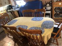 Set of six wooden dining chairs around a table with a yellow tablecloth and blue placemats. Four side chairs without arms and two armchairs visible.