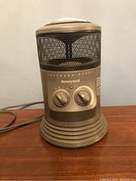 Front view of used Honeywell space heater showing two control knobs, mesh heating area, flared grooved base, beige plastic housing.