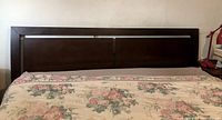 Dark brown king size headboard against wall with floral bedding below, showing panel design and condition.