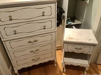 Front view of white dresser and matching beside table showing gold painted detailing and drawer fronts