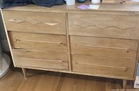 Front view of the natural wood dresser showing six drawers with carved diamond-shaped design on the top drawers and metal drawer handles.