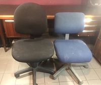 Overview of two medium-sized adjustable height office chairs without arms, one black fabric and one blue fabric, both showing stains and wear