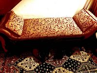 Full length side view of wooden settee bench with detailed patterned upholstery and cushions on visible carpeted floor.