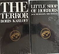 Front view of two sealed vintage VHS tapes: The Terror and Little Shop of Horrors, both with black cover and gold Video Era logo.