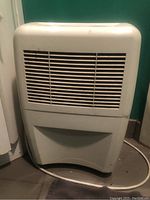 Front view of white Whirlpool dehumidifier showing ventilation grilles and cord on floor.