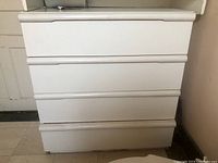 Front view of white dresser with four drawers, showing overall shape and condition including visible damage on drawer front.