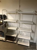 Two white metal shelving units placed side by side with perforated open shelves and some items stored on the bottom shelf of the left unit.