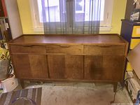 Full view of walnut sideboard showing 3 drawers on top and 3 doors beneath with pointed legs.