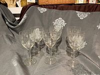 Six vintage clear wine glasses with etched diamond and line patterns displayed against a gray patterned fabric background.