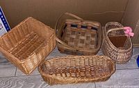 Four vintage baskets shown together in cardboard box on wooden floor, showcasing various shapes and weaving styles.