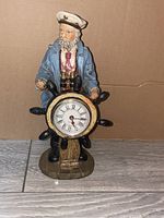 Front view of ceramic ship captain figurine at ship wheel with embedded clock, showing condition and details.
