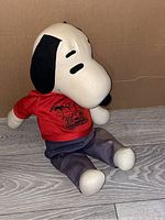 Front and side views of large vintage 1960s stuffed Snoopy doll sitting on a wood-textured surface against a plain background, showing details of face, clothing, and wear.
