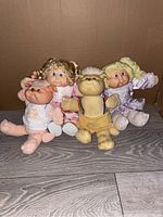 Four Cabbage Patch dolls grouped on floor against cardboard background confirming quantity and style.