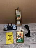 Photo of six vintage items including mirror, salt and pepper shakers, first aid kit, velcro package, and WWII bunker phone handset arranged on a surface against cardboard background.