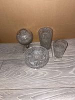 Four vintage or antique cut glass crystal pieces arranged on wooden surface, showing side and top views to detail cut patterns and shapes.