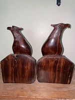Pair of dark wood carved hawk bookends viewed from a side angle showing the front and side profile of the hawks and bases.