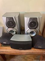 Front view of whole set showing all five Aiwa speakers (two large, two small satellites, one center channel) arranged on a wooden surface.