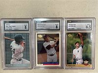 Front view of three Derek Jeter baseball cards graded 8, 8, and 6.5 in protective cases