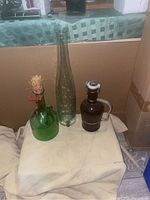 Photo showing three distinct large decorative glass bottles on a cloth with cardboard background