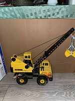Side view of the vintage Tonka yellow metal crane toy showing the crane arm with yellow grab bucket, black cables and body with Tonka logo.