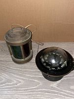 Two vintage maritime items on wood surface: a ships lantern lamp and a black metal compass.