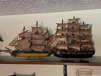 Pair of vintage wooden ship models on a wooden shelf against a wall, showing full side view of both ships.