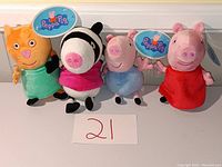 Four Peppa Pig themed plush dolls including Candy Cat, Zoe Zebra, George Pig, and Peppa Pig with tags showing the brand and numbered label card in front.