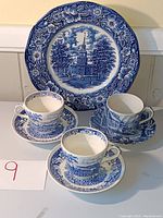 Full view of one large dinner plate with blue and white floral border and tea cups and saucers in front