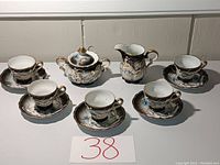 Overview of entire tea set showing five teacup and saucer pairs, sugar bowl with lid, and creamer jug arranged on a white surface.
