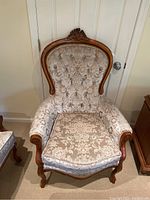 Front view of armchair showing carved crest, tufted back, and seat cushion
