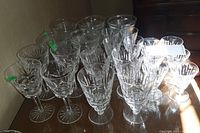 Various clear glassware with different etched and cut patterns arranged in groups on a table, showing some glasses with stemmed bases.