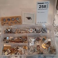 Full view of plastic organizer box with multiple compartments containing cuff links, tie clips, lapel pins, and a folding pocket knife.