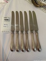 Six butter cutters with sterling silver handles and stainless steel blades, showing full set and layout.