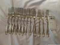 Full view of all twelve sterling forks laid side by side on white background with lot tag